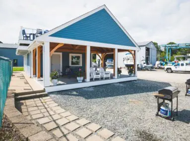 two small barbecues in front of a small building with white chairs on the porch