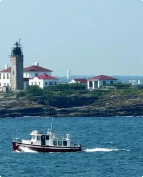 boat with a stone light house and white and red buildings behind it