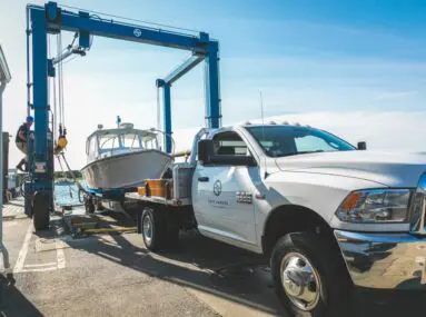 white truck with safe harbor logo on the side, in the process of receiving a boat from a lift