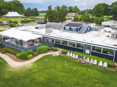Blue restaurant with outdoor covered patio seating and row of white Adirondack chairs on lawn