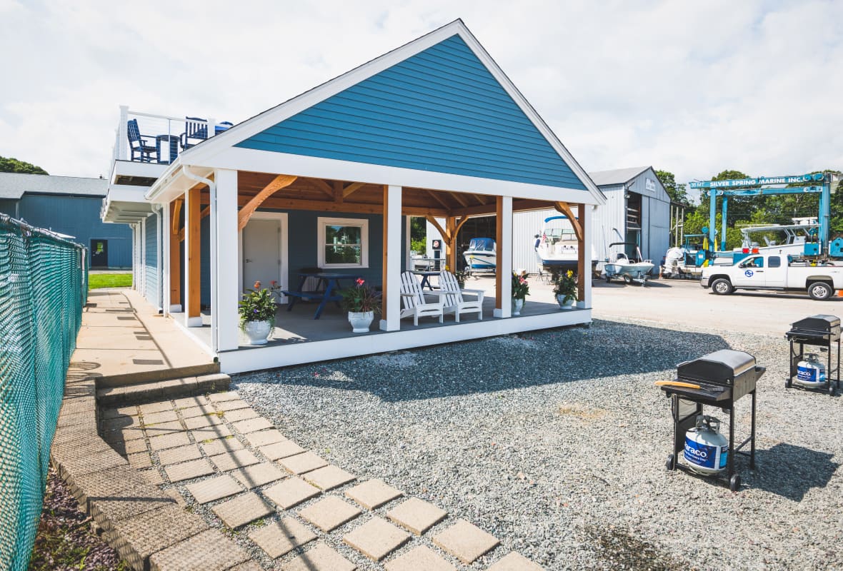 two small barbecues in front of a small building with white chairs on the porch