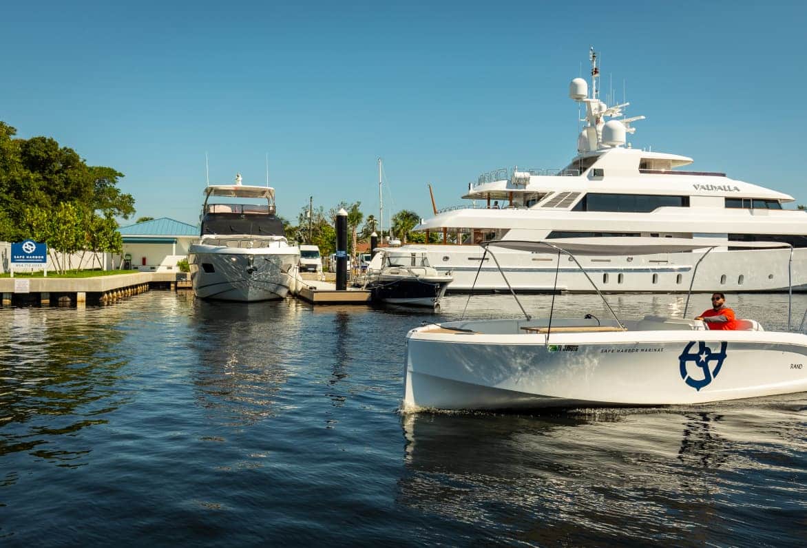 safe harbor boat cruising along in front of yachts docked behind it