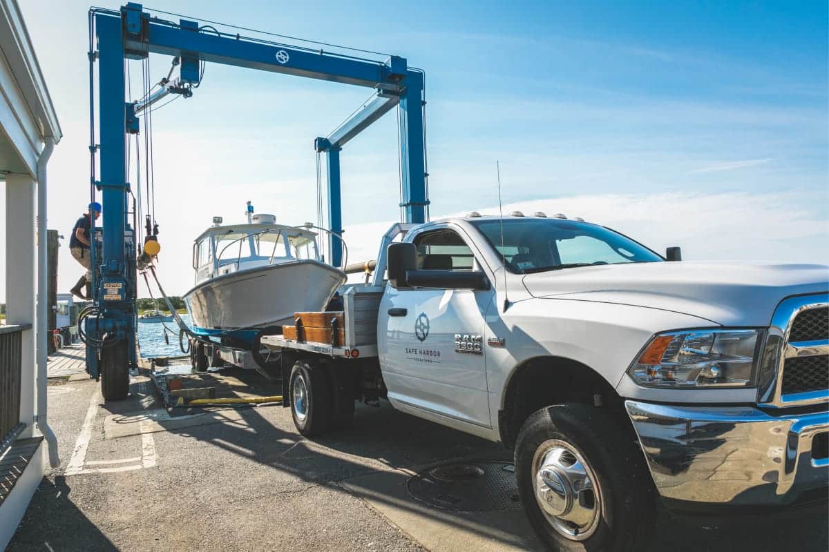white truck with safe harbor logo on the side, in the process of receiving a boat from a lift
