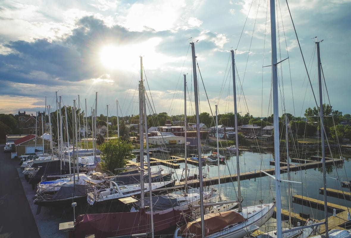 lots of sailboats docked at marina and sun shining through clouds