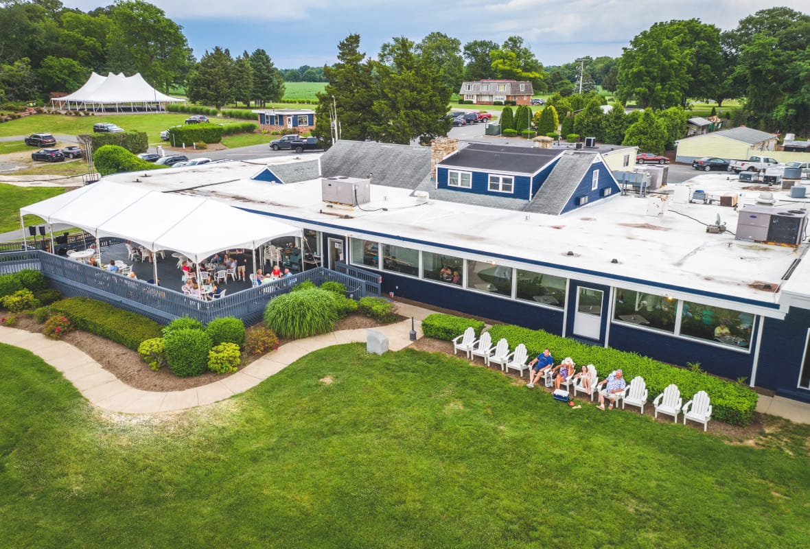 Blue restaurant with outdoor covered patio seating and row of white Adirondack chairs on lawn
