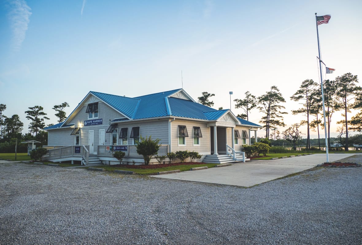 Small building with blue roof surrounded by trees and a gravel parking lot