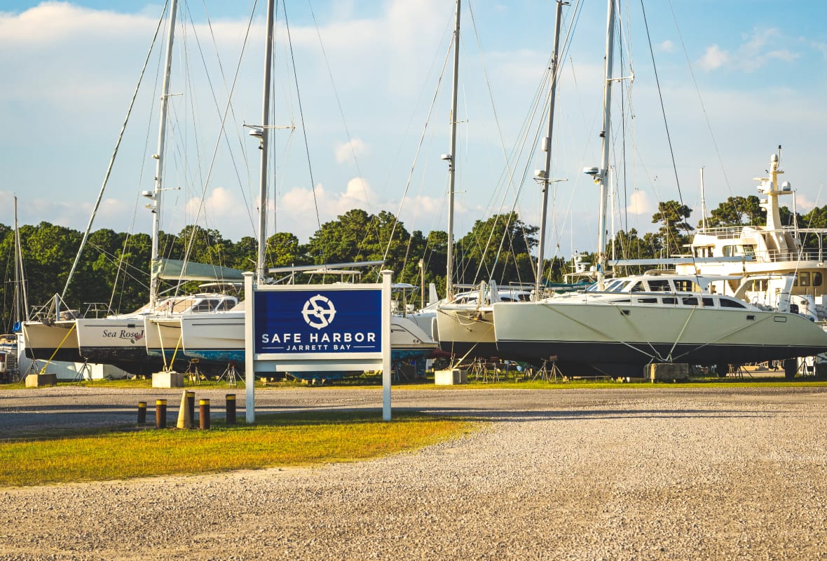 Safe Harbor Jarrett Bay sign with sailboats docked on land behind it